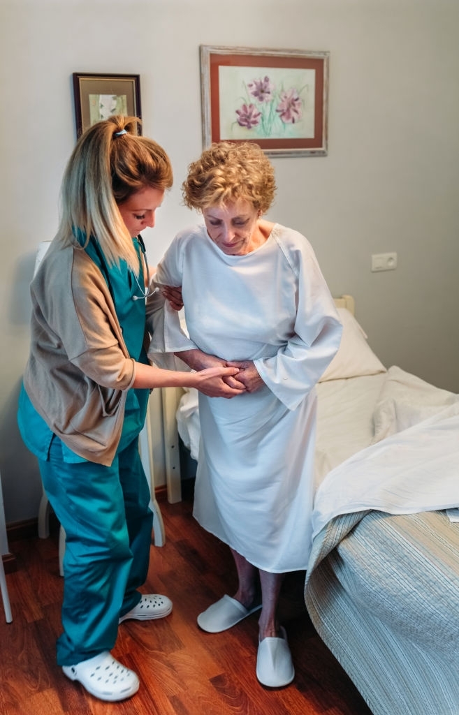 a female medical professional helping an elderly woman stand and walk