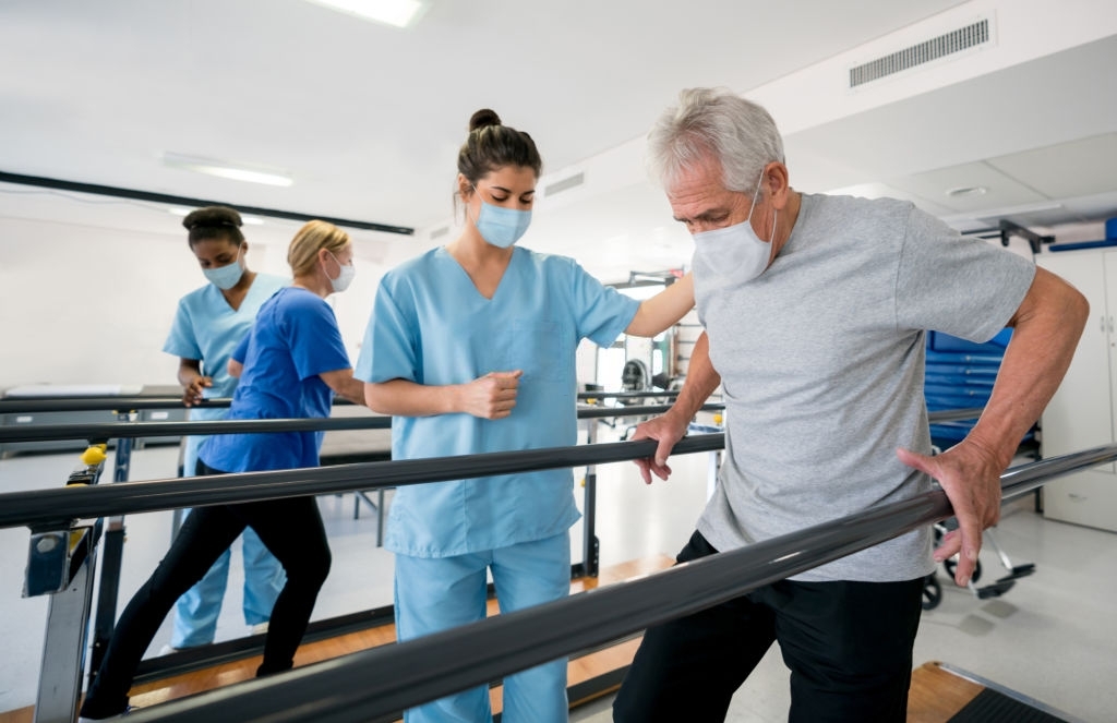a female medical professional helping an elderly man walk using parallel bars