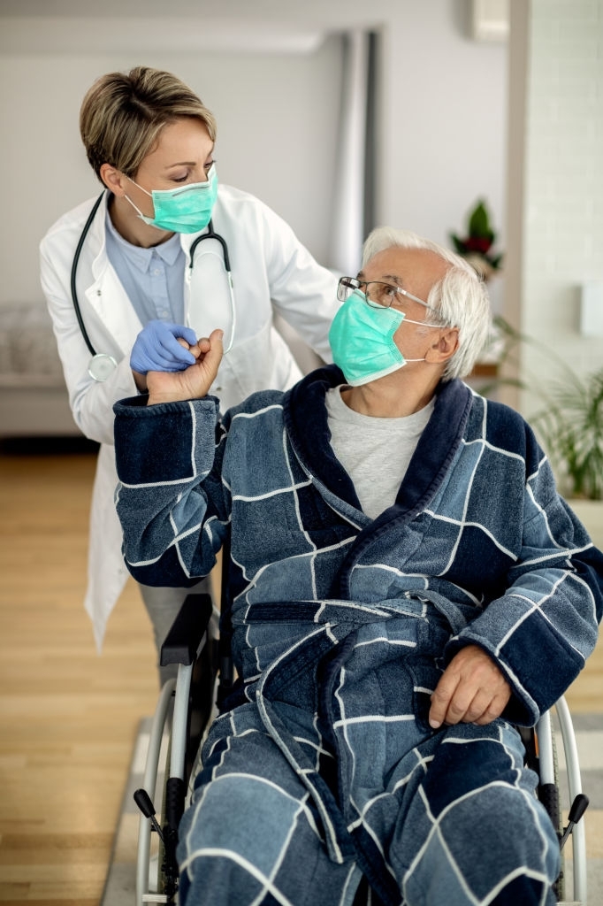 a female medical professional in a white coat and an elderly man in a wheelchair