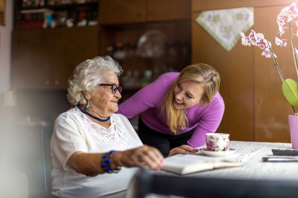 a young woman checking in on an elderly woman who was reading a book